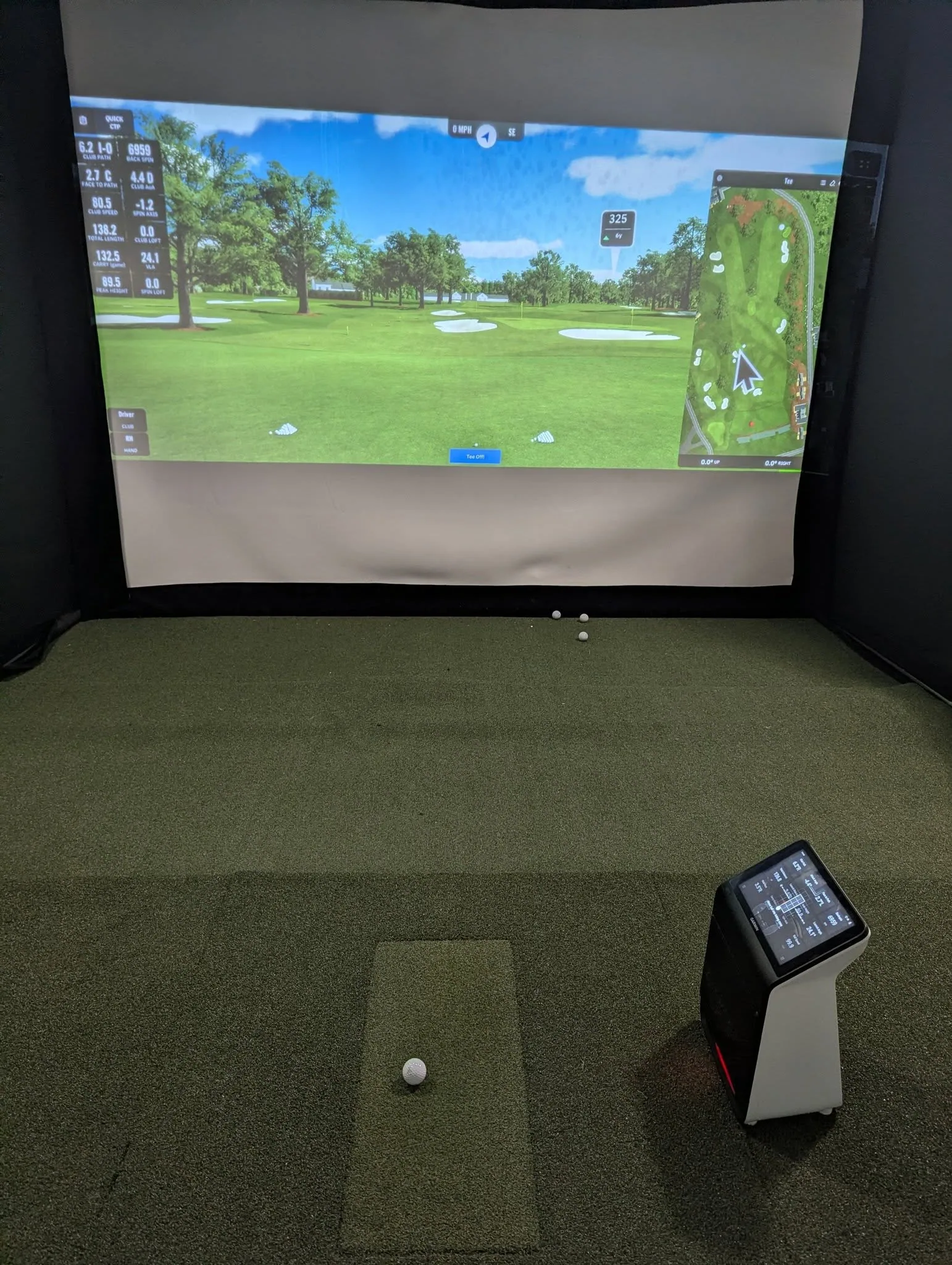 Indoor golf simulator bay with a projected course, hitting mat, golf balls, and launch monitor